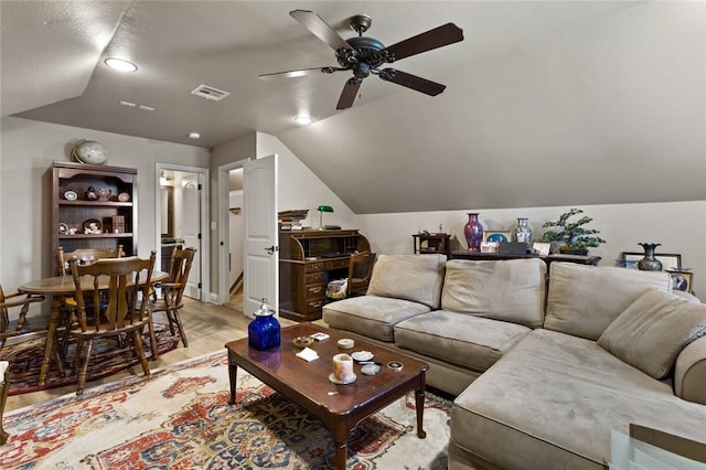 living area featuring lofted ceiling, light wood-style flooring, visible vents, and ceiling fan