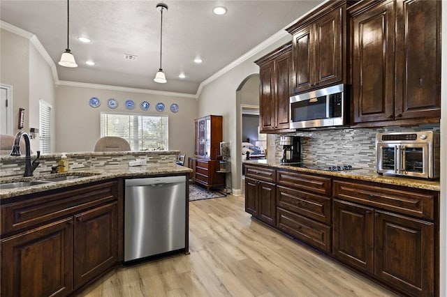 kitchen featuring stainless steel appliances, a sink, hanging light fixtures, dark brown cabinets, and light stone countertops