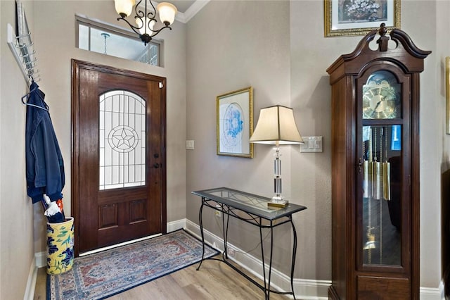 foyer with baseboards, ornamental molding, light wood-type flooring, and a notable chandelier