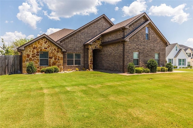 view of front of house featuring stone siding, brick siding, fence, and a front lawn