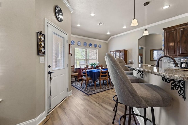 kitchen with crown molding, hanging light fixtures, light wood-style flooring, dark brown cabinetry, and dark stone counters