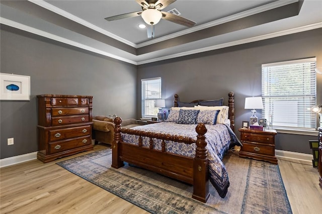 bedroom featuring a tray ceiling, crown molding, light wood-style flooring, and baseboards