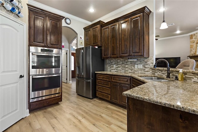 kitchen with arched walkways, dark brown cabinets, appliances with stainless steel finishes, decorative backsplash, and decorative light fixtures