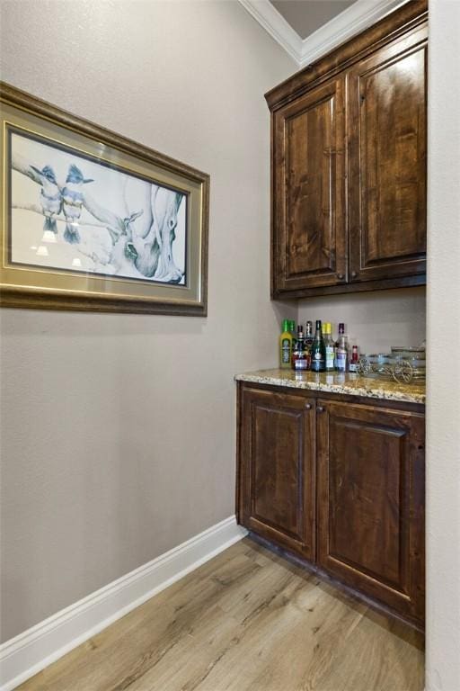 bar featuring a bar, ornamental molding, light wood-type flooring, and baseboards