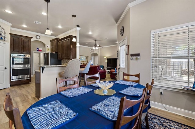 dining room with light wood finished floors, baseboards, visible vents, a ceiling fan, and crown molding