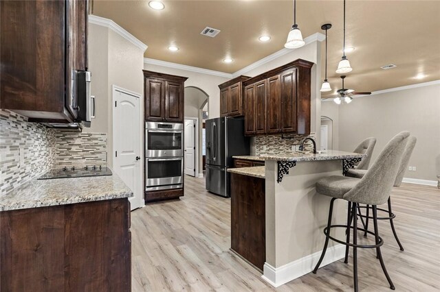 kitchen featuring light stone counters, a breakfast bar, arched walkways, freestanding refrigerator, and a peninsula