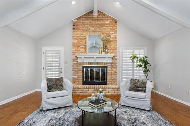 living room with a healthy amount of sunlight, hardwood / wood-style floors, lofted ceiling with beams, and a brick fireplace