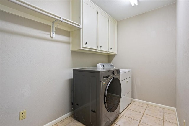 clothes washing area with washer and clothes dryer, light tile patterned floors, and cabinets