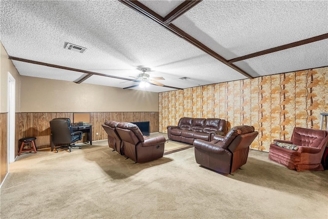 carpeted living room with beam ceiling, a textured ceiling, ceiling fan, and wood walls