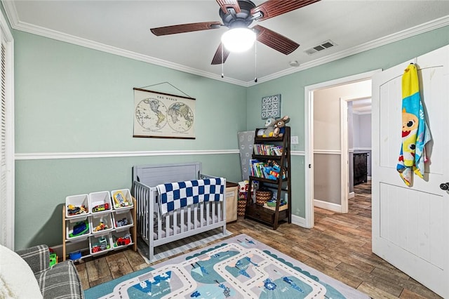 bedroom featuring ceiling fan, a crib, ornamental molding, and hardwood / wood-style floors