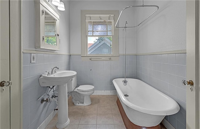 bathroom featuring tile patterned floors, toilet, a tub, and tile walls