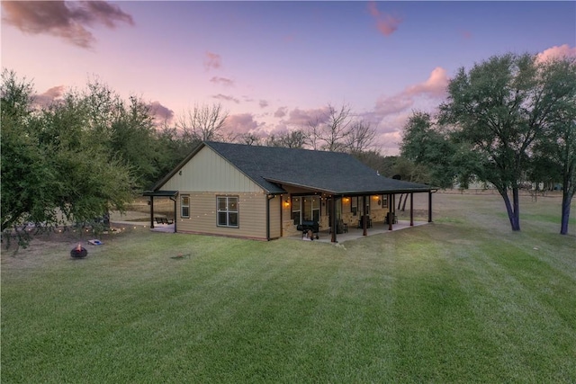 back house at dusk featuring a lawn and a patio