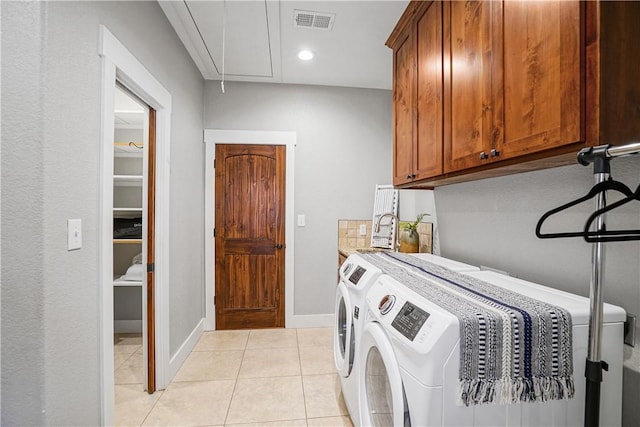 clothes washing area featuring cabinets, light tile patterned floors, and washing machine and clothes dryer