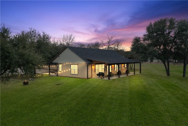 back house at dusk featuring a lawn and a patio area