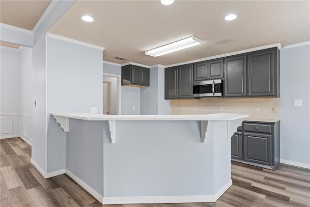 kitchen featuring gray cabinetry, a kitchen breakfast bar, ornamental molding, and light hardwood / wood-style flooring