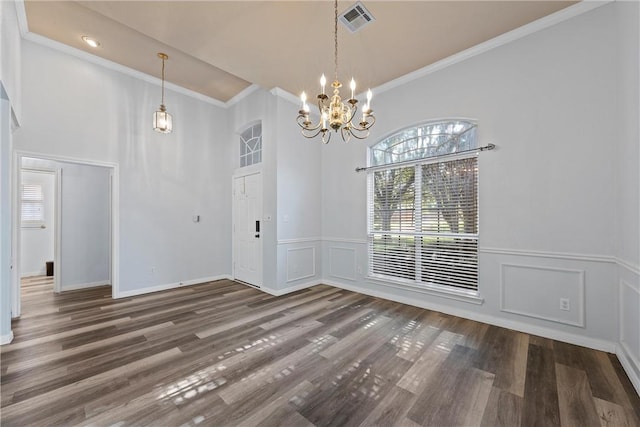 unfurnished dining area featuring dark hardwood / wood-style flooring, ornamental molding, a towering ceiling, and a chandelier