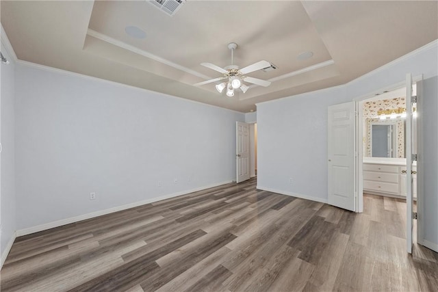 unfurnished bedroom featuring ensuite bath, a raised ceiling, ceiling fan, crown molding, and hardwood / wood-style flooring