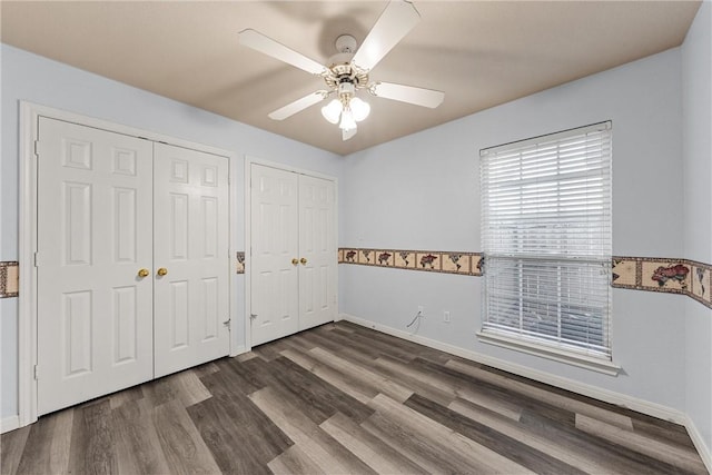 unfurnished bedroom with dark hardwood / wood-style floors, ceiling fan, and multiple closets