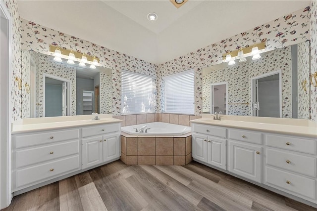 bathroom with tiled tub, vanity, wood-type flooring, and vaulted ceiling