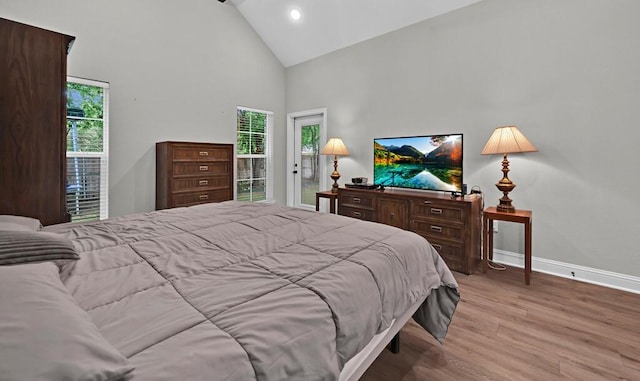 bedroom featuring multiple windows, high vaulted ceiling, and light wood-type flooring