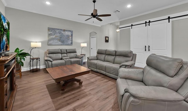 living room with hardwood / wood-style flooring, ceiling fan, a barn door, and crown molding