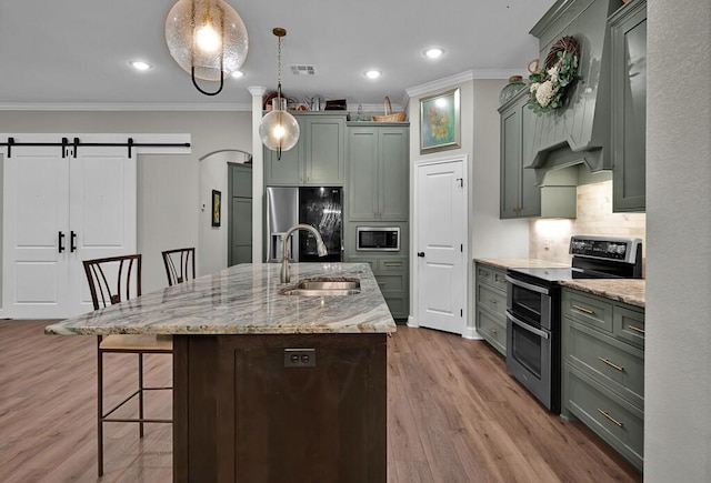 kitchen with sink, stainless steel appliances, a barn door, a large island with sink, and pendant lighting