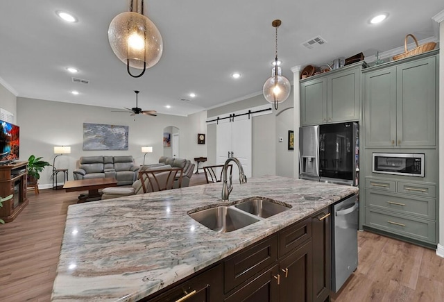 kitchen featuring light stone countertops, sink, stainless steel appliances, hanging light fixtures, and a barn door