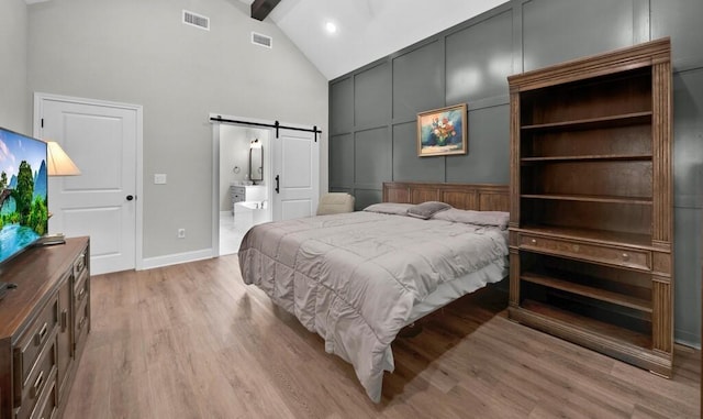 bedroom featuring high vaulted ceiling, a barn door, connected bathroom, beamed ceiling, and light hardwood / wood-style floors