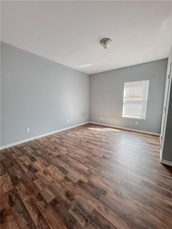 spare room with baseboards and dark wood-style flooring