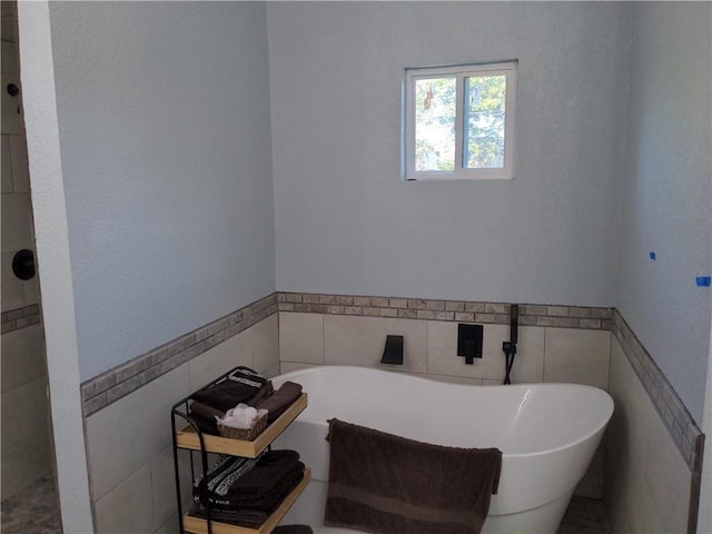 bathroom with a tub to relax in and tile walls