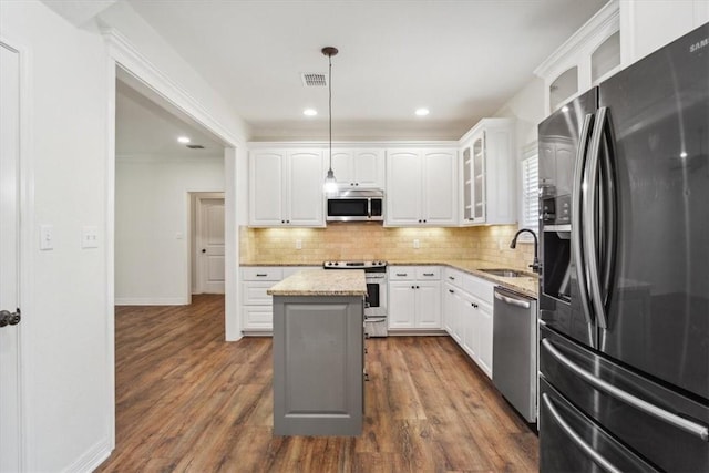 kitchen with stainless steel appliances, sink, pendant lighting, white cabinetry, and a kitchen island