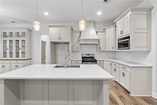 kitchen featuring pendant lighting, an island with sink, stainless steel appliances, and custom range hood