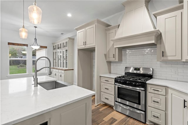 kitchen with custom exhaust hood, sink, pendant lighting, hardwood / wood-style flooring, and stainless steel range with gas stovetop