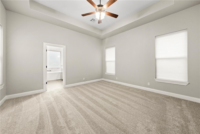 carpeted spare room featuring ceiling fan, a healthy amount of sunlight, and a tray ceiling