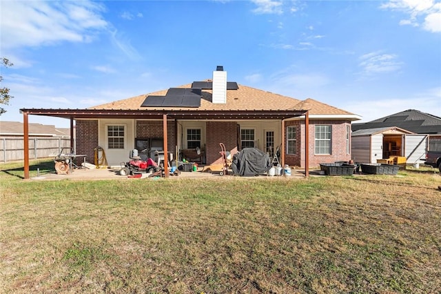 rear view of house with solar panels, a storage shed, a yard, and a patio