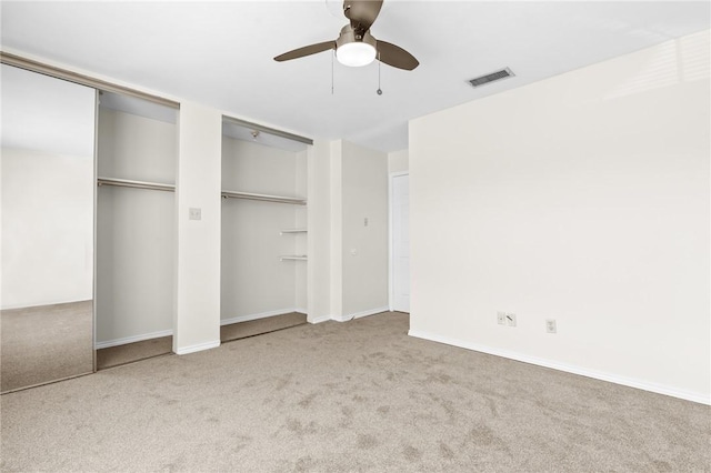 unfurnished bedroom featuring ceiling fan, light colored carpet, and two closets