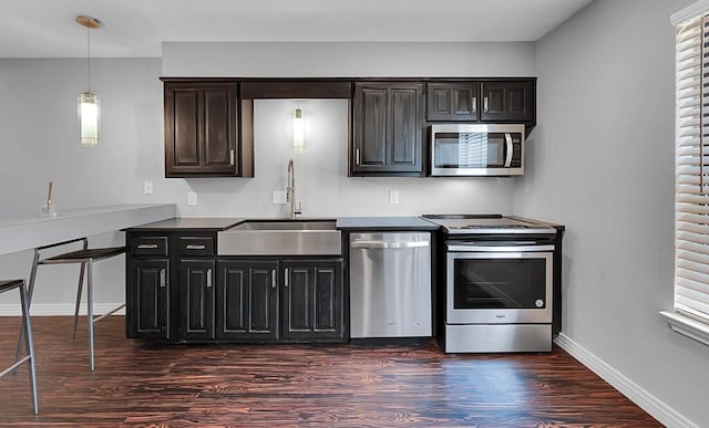 kitchen featuring pendant lighting, a sink, dark wood finished floors, stainless steel appliances, and baseboards