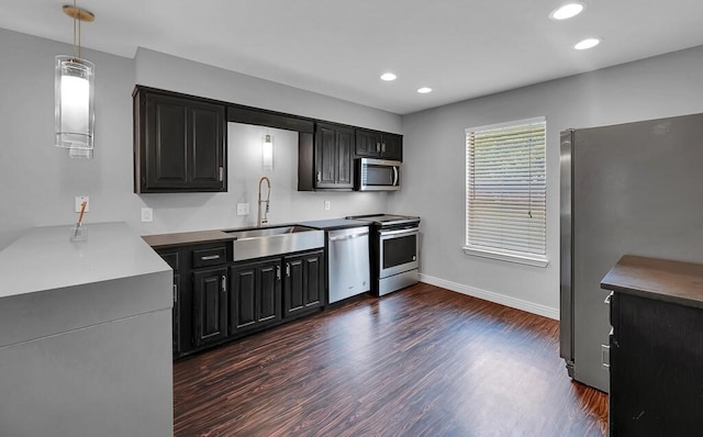 kitchen featuring dark cabinetry, dark wood-type flooring, appliances with stainless steel finishes, and a sink