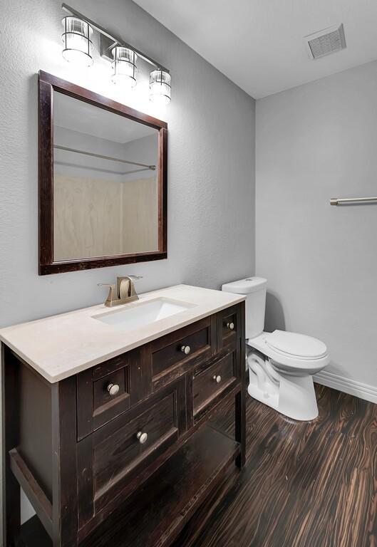 bathroom with vanity, wood finished floors, visible vents, baseboards, and toilet