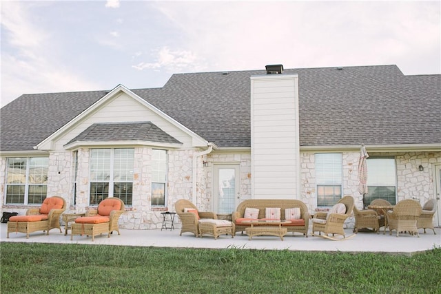 back of house with a patio, a chimney, a shingled roof, outdoor lounge area, and stone siding