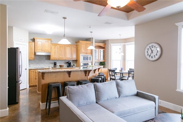 kitchen featuring under cabinet range hood, visible vents, a kitchen breakfast bar, appliances with stainless steel finishes, and light brown cabinetry