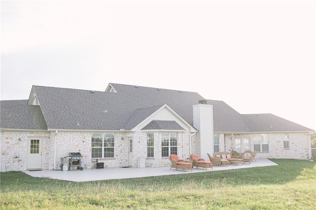 back of property featuring a yard, a chimney, a patio area, and roof with shingles