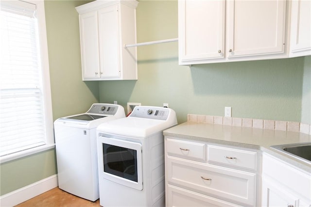 washroom featuring washing machine and dryer, cabinet space, and baseboards