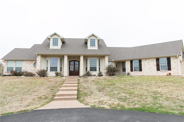 cape cod-style house featuring stone siding, a shingled roof, a front lawn, and french doors