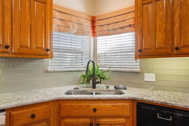 kitchen with black dishwasher, tasteful backsplash, light stone counters, and sink