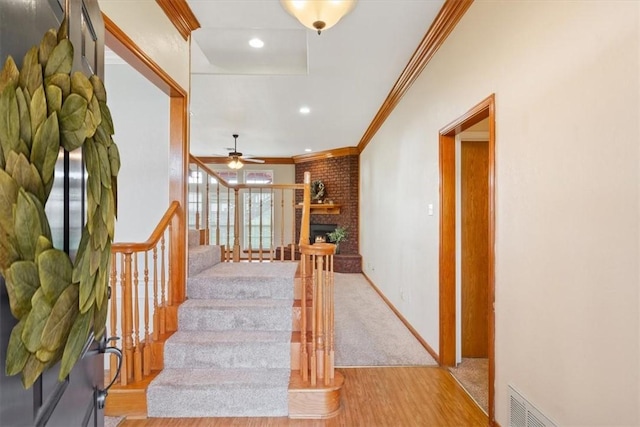 stairs with wood-type flooring, a brick fireplace, ceiling fan, and ornamental molding