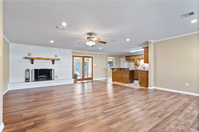 unfurnished living room with sink, light hardwood / wood-style flooring, ornamental molding, and a brick fireplace