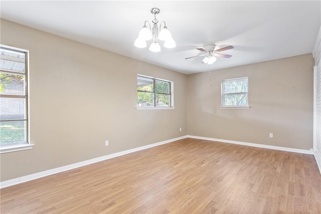 spare room with ceiling fan with notable chandelier, light hardwood / wood-style flooring, and plenty of natural light