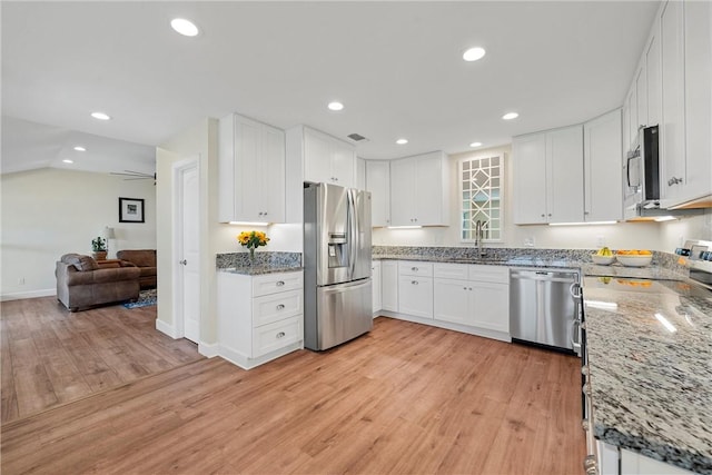 kitchen featuring white cabinetry, sink, light hardwood / wood-style flooring, dark stone countertops, and appliances with stainless steel finishes