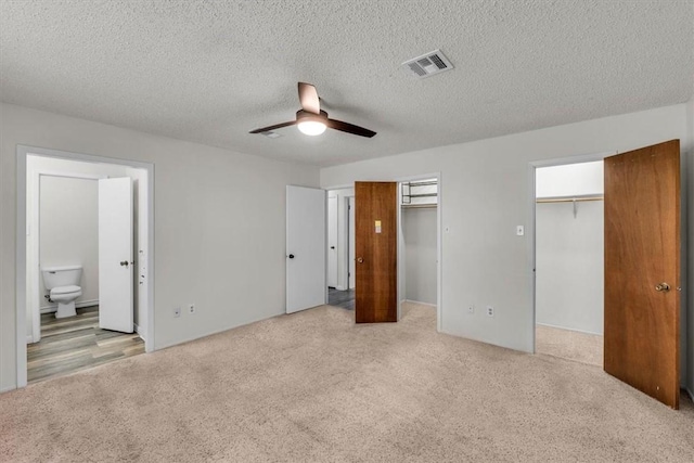 unfurnished bedroom with ensuite bath, ceiling fan, light carpet, and a textured ceiling